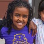 Five elementary students sit together in a courtyard and smile for a photo