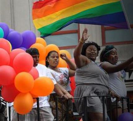 Pride Parade participants along with balloons and rainbows on a float