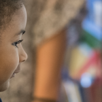 A young student works on a math problem while standing at a white board in a classroom.