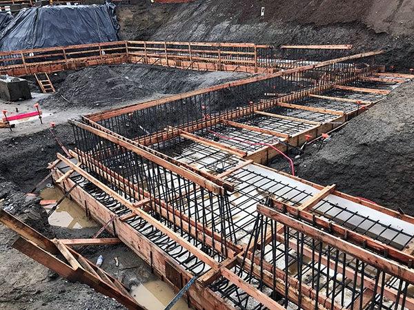 a construction site has steep soil walls and a zig-zag of concrete forms with rebar at the bottom and up the sides