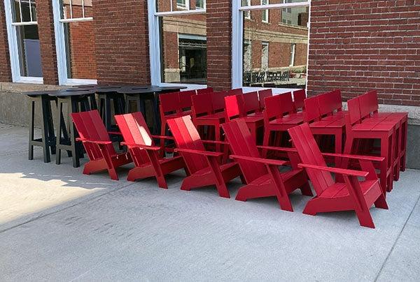 red chairs and stools, and black tall tables sit by a brick building with windows