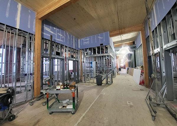 interior of a building under construction with high wood covered ceilings, wood post and beams, and metal wall studs with wallboard on the upper part of the wall