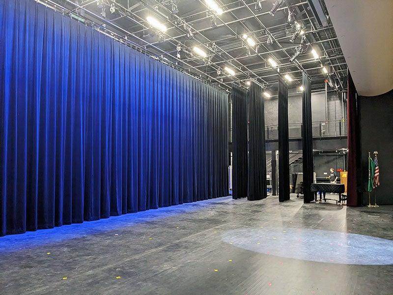 a stage with lighting in the ceiling has blue curtains