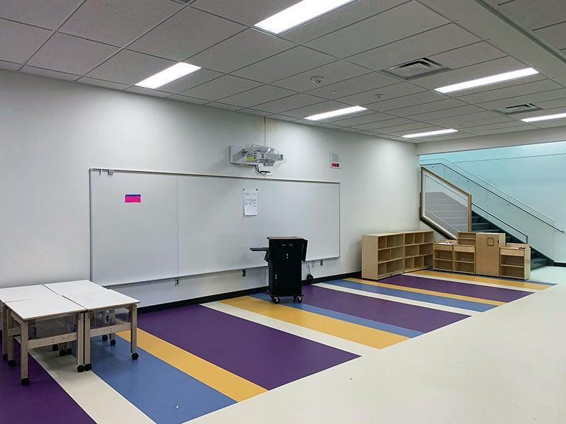 a common area is defined by a striped floor and a learning wall and teacher station