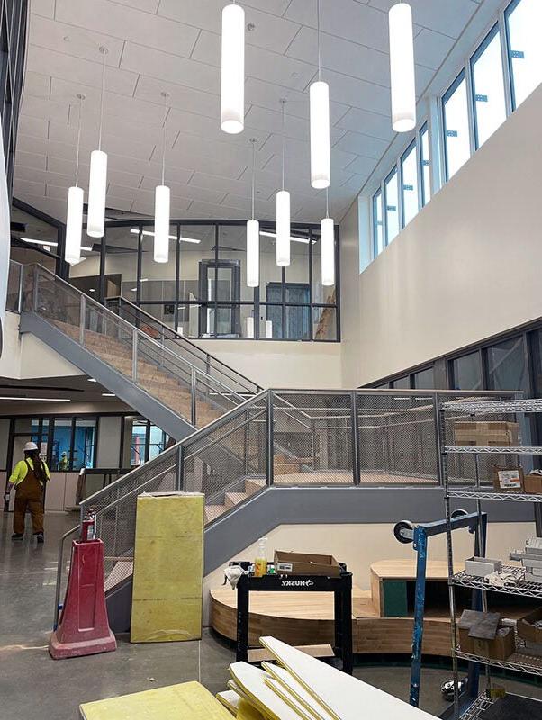 tube shaped light fixtures hang from a high ceiling in a two story space with a stairway