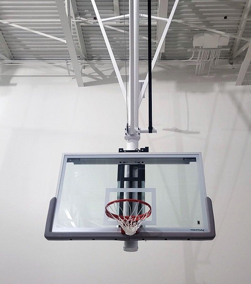 a basketball hoop with clear backboard hangs from ceiling in a large room