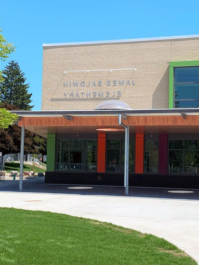 part of a two story building with a canopy that has wood edge and windows. a sign on the building says James Baldwin Elementary