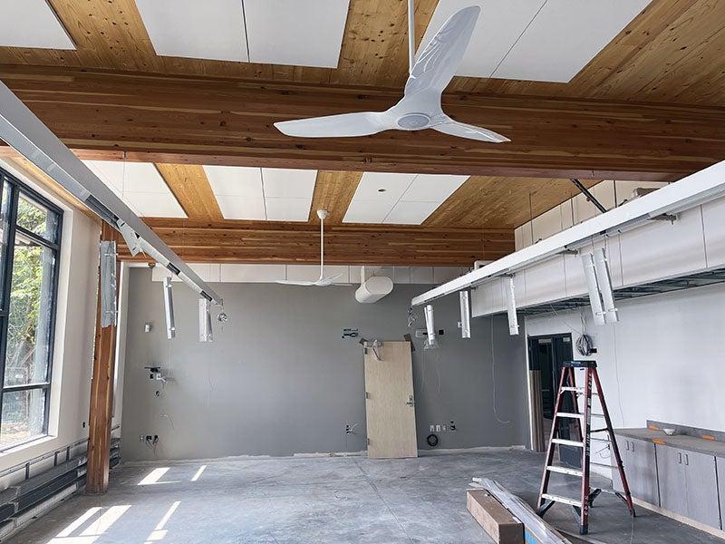 a room with windows on one wall and wood beams with a ceiling fan and partially installed light bars