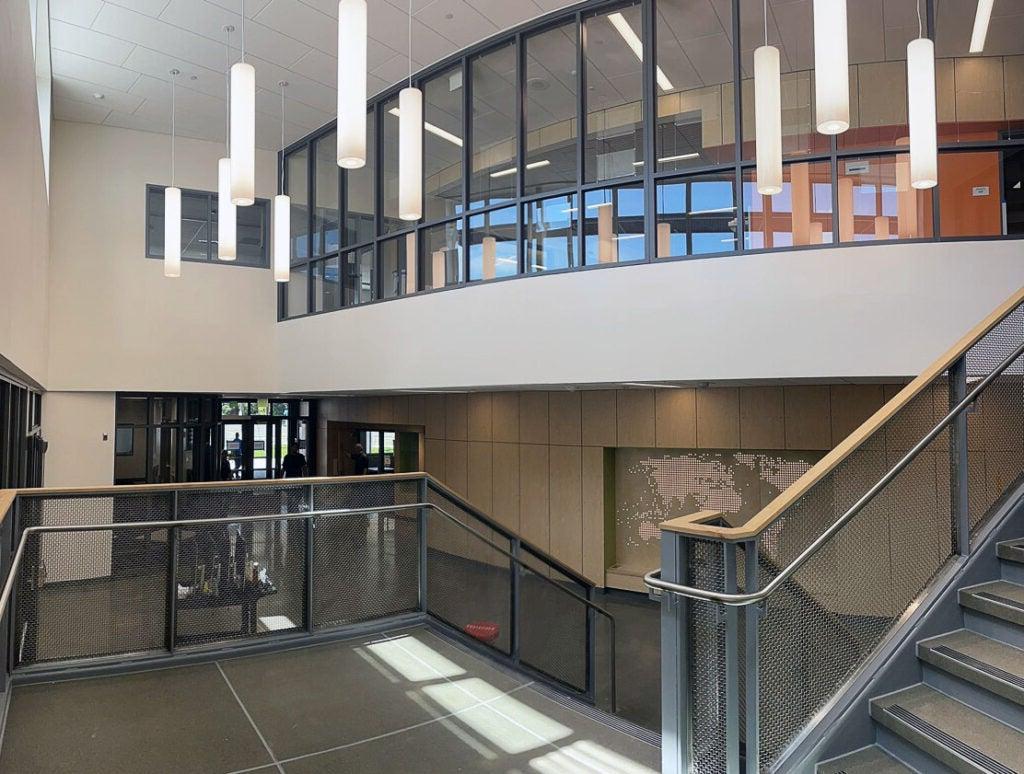 view from halfway up stairs on a landing. you can see part of the second floor with a curved glass wall and part of the lower floor.