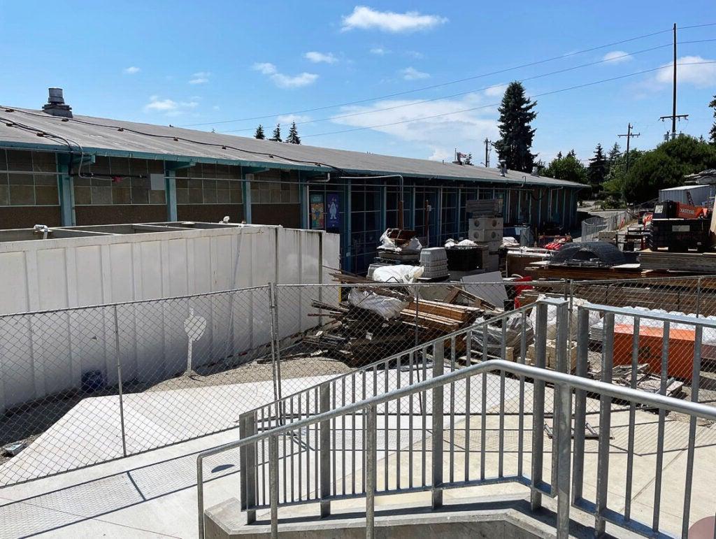 outdoor looking toward a long low building with a stairway, concrete walk, and construction materials in front of it