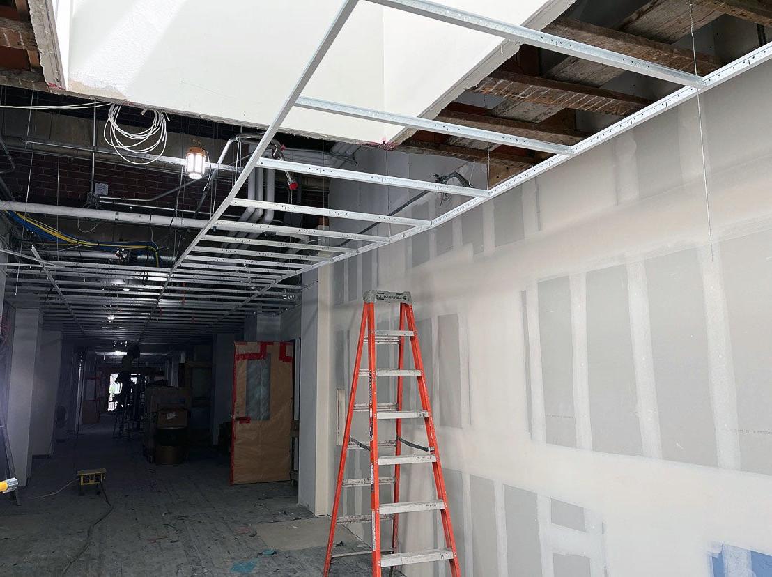 an unfinished hallway with one wall showing wallboard that is taped and mudded. The ceiling is open with a metal grid partially installed