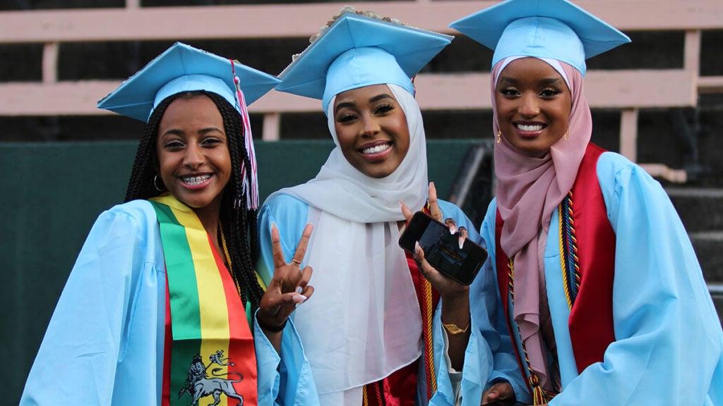 Three graduates smile for a photo in cap and gown