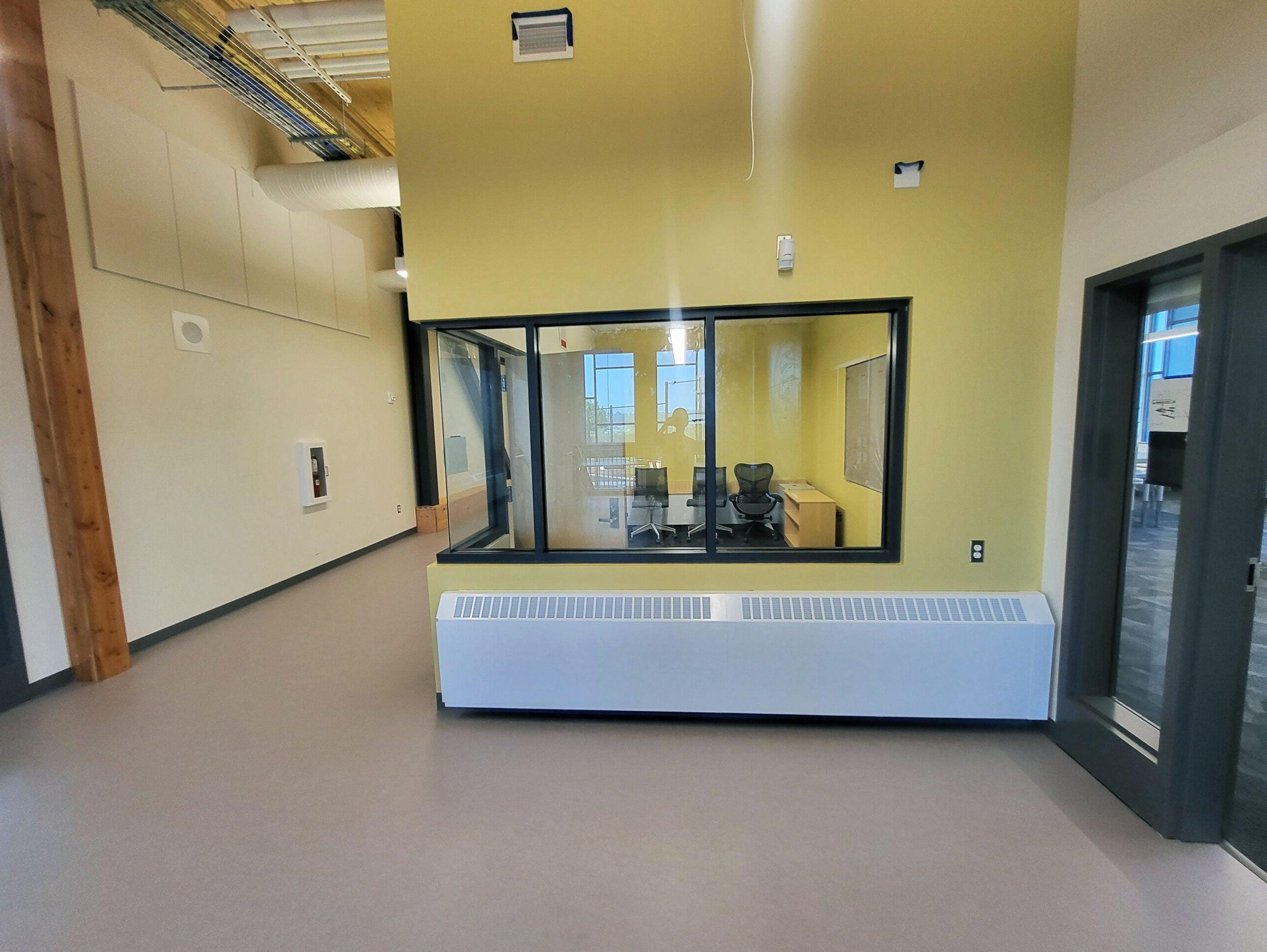 a window in a wall shows a small room with three chairs, a table, and a bookshelf