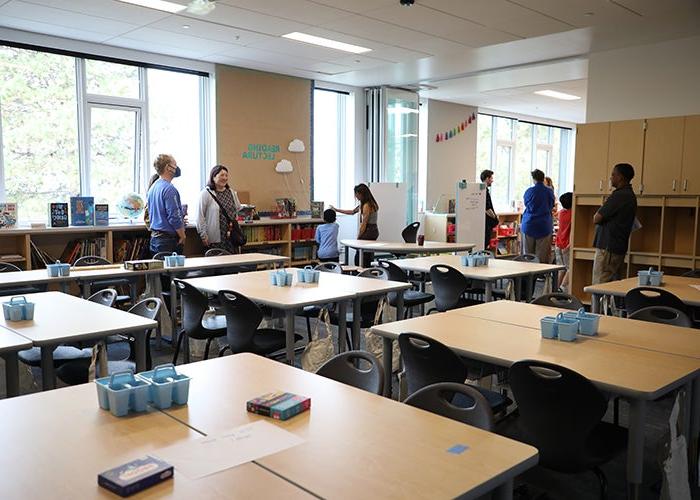 a classroom with groups of tables and a wall that is open to another classroom