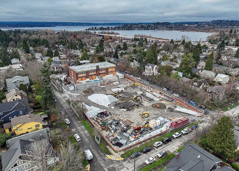 aerial view of a construction site with a brick building at one end and a view of a lake in the distance