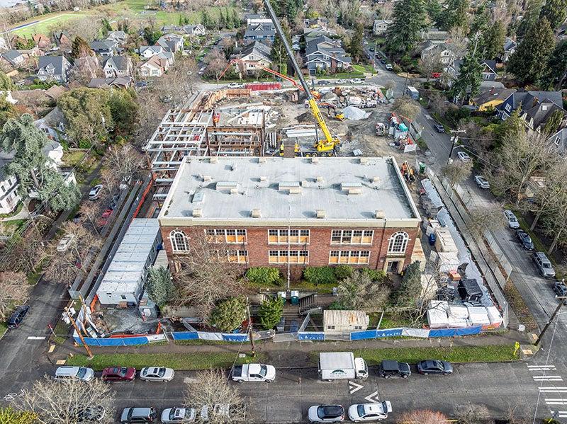 aerial showing a rectangular brick building with construction happening behind it including a crane