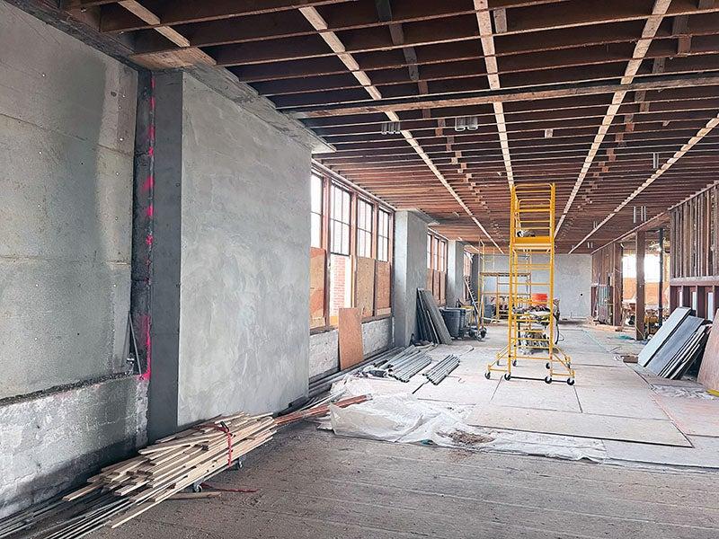 a long room with rafters showing and a concrete wall next to some windows