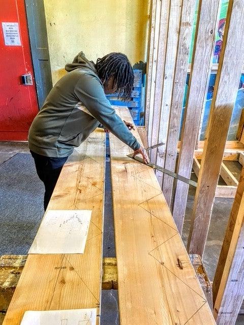 Student measuring wood for cutting with saw