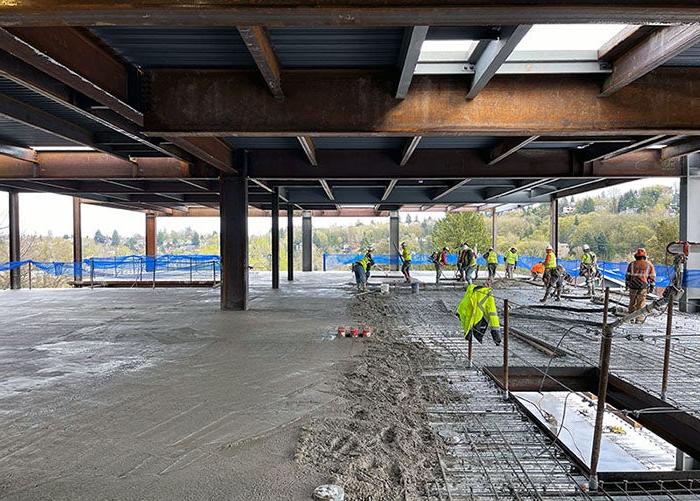 wet concrete covers the floor of a building with steel framing. workers in safety equipment are smoothing the concrete