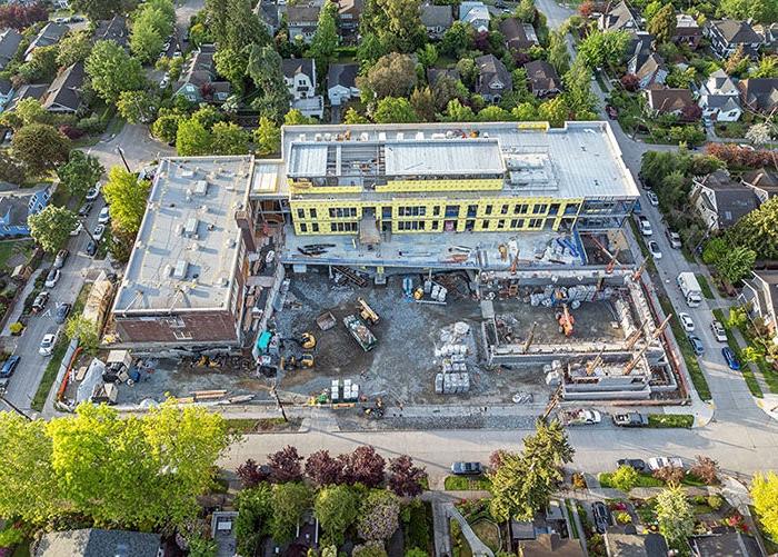 a construction site with a brick building forming an L with a new building. a partially built building is at the other end of the new building