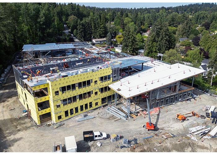 a large building under construction with a 3 story section covered in yellow material with writing and a section that has a sloped roof