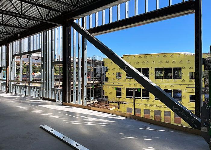 looking out through a wall framing without walls toward another building that has yellow sheathing on it