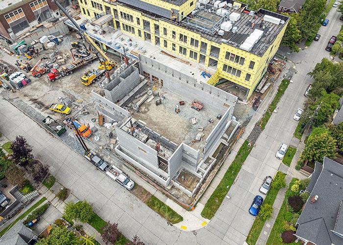 aerial with view of a concrete block building on the corner of the construction site with the new addition above it and part of the historic building to the right