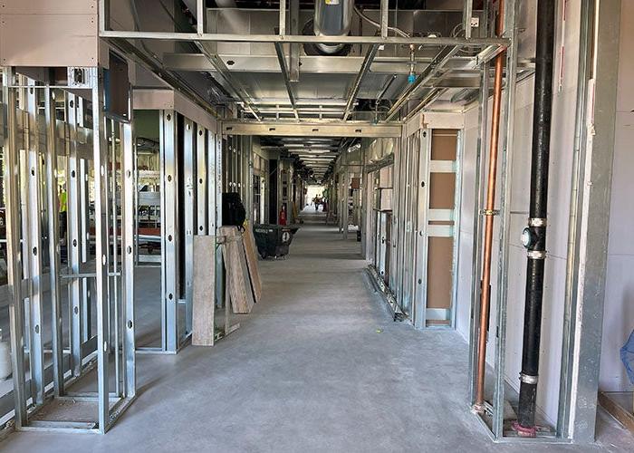 inside a hallway under construction with steel framed walls on each side and utility pipes and conduit showing