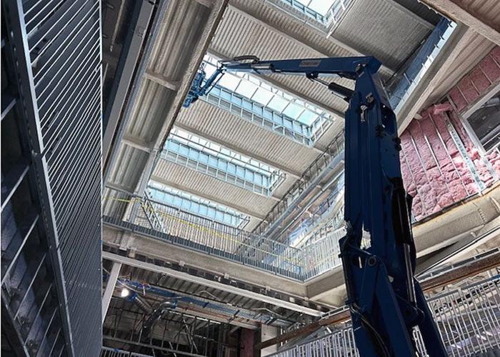 interior of a building under construction looking up toward skylights several floors above. there are metal studs and railings on the side and a lift is raised to the top floor walls